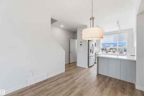 The open concept living area features hardwood style flooring, a contemporary drum pendant light fixture, and a kitchen island with a light-colored countertop - 49 100 Jensen Lakes Boulevard, St. Albert, AB - Indoor Photo Showing Kitchen