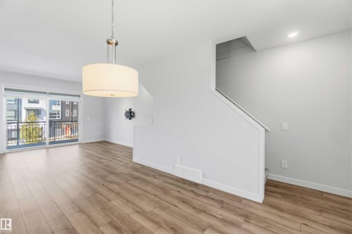 Bright living space with hardwood style flooring, a modern drum pendant light, and a sliding glass door leading to a balcony - 49 100 Jensen Lakes Boulevard, St. Albert, AB - Indoor