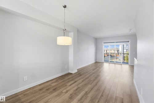 Bright living space featuring light wood-look flooring, a modern drum pendant light, and a sliding glass door leading to an outdoor balcony - 49 100 Jensen Lakes Boulevard, St. Albert, AB - Indoor