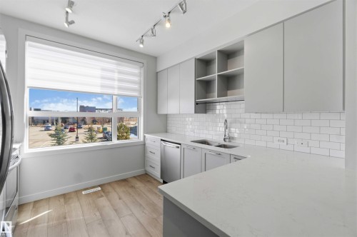 The kitchen features light wood-style flooring, white subway tile backsplash, light gray cabinetry, and light-colored countertops - 49 100 Jensen Lakes Boulevard, St. Albert, AB - Indoor Photo Showing Kitchen With Double Sink With Upgraded Kitchen