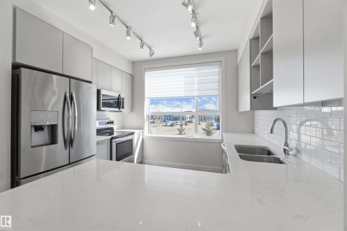 The kitchen features stainless steel appliances, white cabinetry, a double sink, and a window providing natural light - 49 100 Jensen Lakes Boulevard, St. Albert, AB - Indoor Photo Showing Kitchen With Double Sink With Upgraded Kitchen