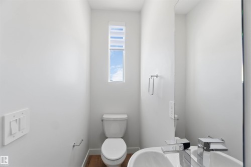 The bathroom features a toilet, a window with blinds, a wall-mounted mirror, and a sink with a modern faucet - 49 100 Jensen Lakes Boulevard, St. Albert, AB - Indoor Photo Showing Bathroom