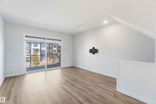 This room features light-toned flooring and a spacious sliding glass door that opens to a balcony with metal railings - 49 100 Jensen Lakes Boulevard, St. Albert, AB - Indoor Photo Showing Other Room