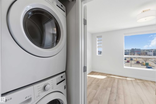 Laundry area with a stacked washer and dryer, adjacent to a room featuring light-toned flooring, white walls, and bright windows - 49 100 Jensen Lakes Boulevard, St. Albert, AB - Indoor Photo Showing Laundry Room