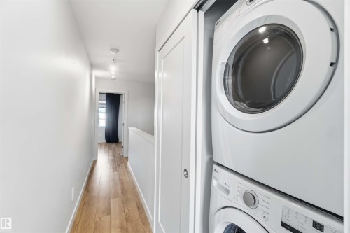 The property features a hallway with light wood flooring and a stacked washer and dryer unit, conveniently located within a closet - 49 100 Jensen Lakes Boulevard, St. Albert, AB - Indoor Photo Showing Laundry Room