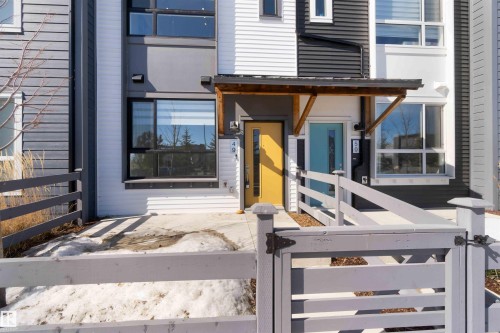The property features an inviting entrance with a bright yellow door, complemented by a light gray fence and a covered entryway - 49 100 Jensen Lakes Boulevard, St. Albert, AB - Outdoor