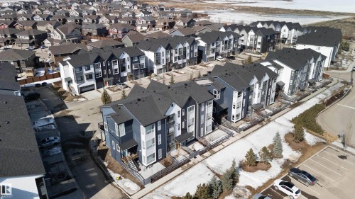 Community featuring a variety of properties with dark roofs and light-colored siding, a paved road, and a parking area - 49 100 Jensen Lakes Boulevard, St. Albert, AB - Outdoor With View