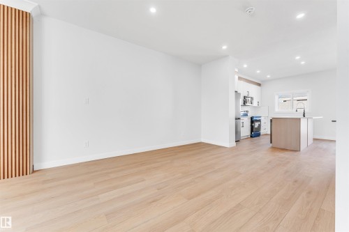 Open-concept living area with light wood flooring, recessed lighting, and a feature wall with vertical wood slats - 10964 157 Street, Edmonton, AB - Indoor