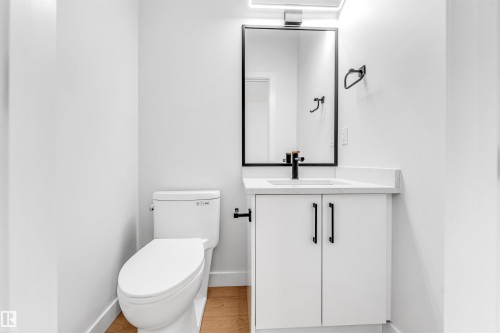 This bathroom features a contemporary vanity with a white countertop and dark hardware, a modern toilet, and light wood flooring - 10964 157 Street, Edmonton, AB - Indoor Photo Showing Bathroom