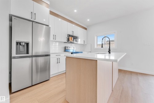 The kitchen features a stainless steel refrigerator, white cabinetry, and light wood flooring - 10964 157 Street, Edmonton, AB - Indoor Photo Showing Kitchen With Upgraded Kitchen