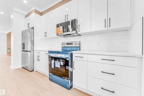 The kitchen features white cabinetry with dark hardware, a stainless steel refrigerator, and a stainless steel microwave - 10964 157 Street, Edmonton, AB - Indoor Photo Showing Kitchen