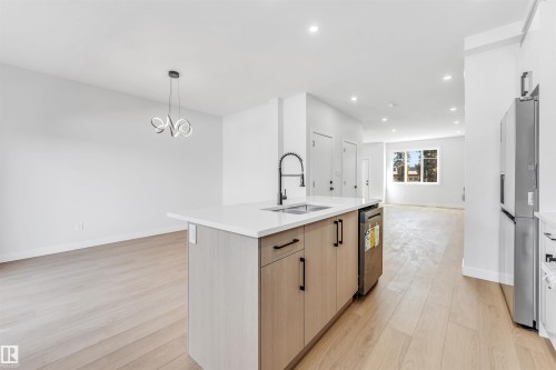 The open concept living area features light wood flooring, a modern kitchen island with a sink and dark faucet, recessed lighting, and a contemporary chandelier - 10964 157 Street, Edmonton, AB - Indoor Photo Showing Kitchen