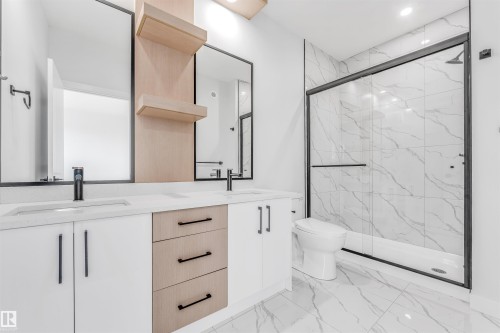 This bathroom features a double vanity with ample storage, framed mirrors, and a spacious shower with a glass enclosure and marble-look tiling - 10964 157 Street, Edmonton, AB - Indoor Photo Showing Bathroom