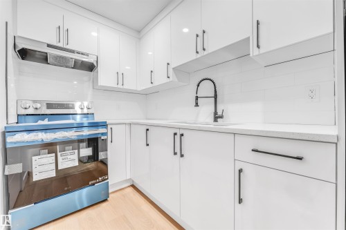The kitchen features white cabinetry, a white subway tile backsplash, light countertops, and a stainless steel range with a matching range hood - 10964 157 Street, Edmonton, AB - Indoor Photo Showing Kitchen