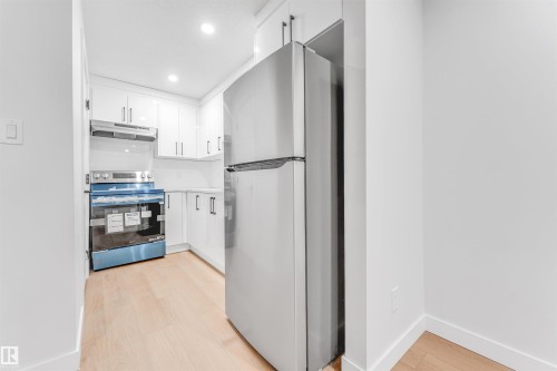 The kitchen features white cabinetry, a stainless steel refrigerator, and a stainless steel range with an overhead vent - 10964 157 Street, Edmonton, AB - Indoor