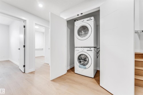 The property features light-toned wood flooring, a stacked washer and dryer, and bright white walls - 10964 157 Street, Edmonton, AB - Indoor Photo Showing Laundry Room