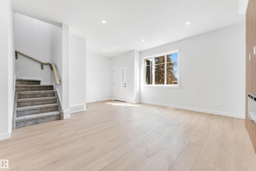 Spacious living area featuring light wood flooring, a large window, recessed lighting, and a staircase with a carpeted runner and wooden handrail - 10964 157 Street, Edmonton, AB - Indoor Photo Showing Other Room