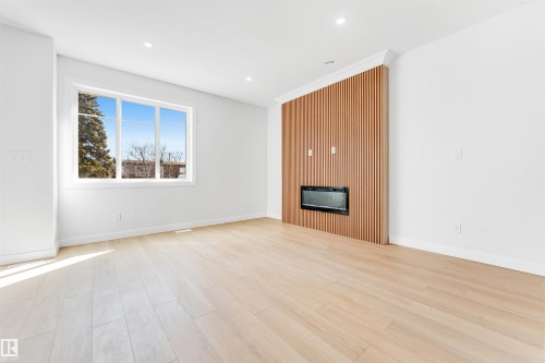 This room features light-toned hardwood flooring, a large window providing natural light, and a fireplace set into a wood-slatted accent wall - 10964 157 Street, Edmonton, AB - Indoor With Fireplace