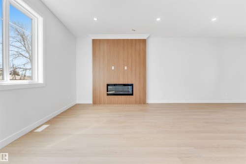 The property features light-colored flooring, a modern fireplace set into a wood-paneled wall, and a large window - 10964 157 Street, Edmonton, AB - Indoor Photo Showing Other Room