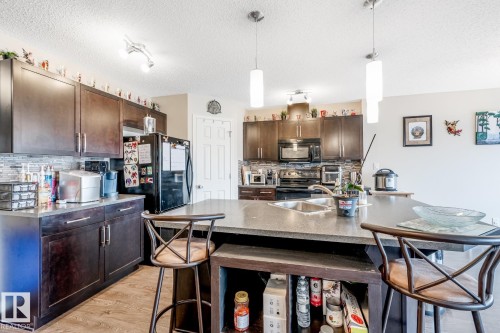 Well-appointed kitchen featuring dark wood cabinetry, a large island with a sink and countertop seating, a tiled backsplash, and recessed lighting - 3109 Carpenter Landing, Edmonton, AB - Indoor Photo Showing Kitchen With Double Sink