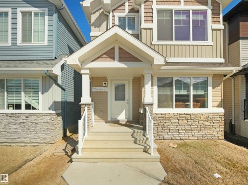 The property features a charming covered porch with white railing accents, a front door with an integrated window, and stone facade detailing on the lower exterior - 1304 14 Avenue, Edmonton, AB - Outdoor