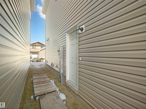 The property features beige siding and a white side entry door with an exterior light fixture - 1304 14 Avenue, Edmonton, AB - Outdoor With Exterior