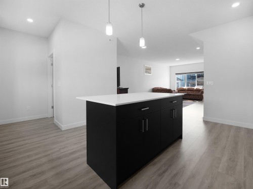 The property features a kitchen island with a white countertop and dark cabinetry, complemented by pendant lighting - 1304 14 Avenue, Edmonton, AB - Indoor Photo Showing Other Room