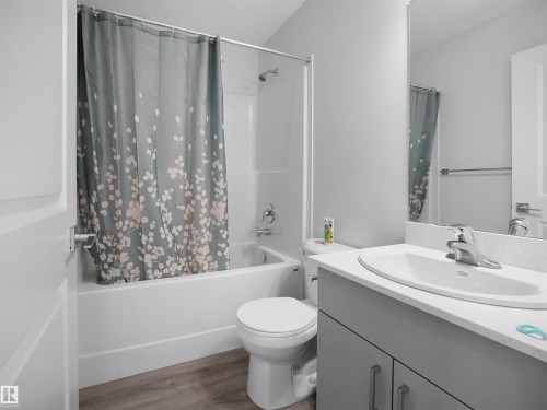 The bathroom features a bathtub with a shower, a toilet, a vanity with an integrated sink, and wood-style flooring - 1304 14 Avenue, Edmonton, AB - Indoor Photo Showing Bathroom