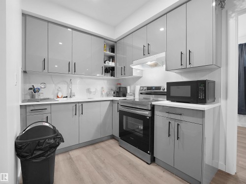 The kitchen features light grey cabinetry with black hardware, a stainless steel oven and range, a microwave, and light-colored countertops - 1304 14 Avenue, Edmonton, AB - Indoor Photo Showing Kitchen
