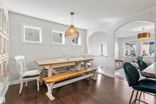 This dining area features rich hardwood flooring, a unique wood dining table with a matching bench, and a woven pendant light fixture - 38 Hewitt Circle, Spruce Grove, AB - Indoor Photo Showing Dining Room