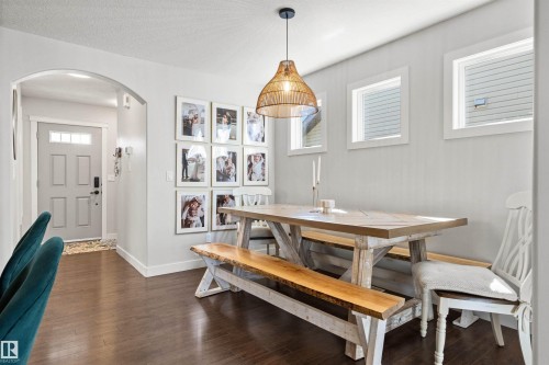 The dining area features dark hardwood flooring, light-colored walls, and a distinctive woven pendant light fixture - 38 Hewitt Circle, Spruce Grove, AB - Indoor Photo Showing Dining Room