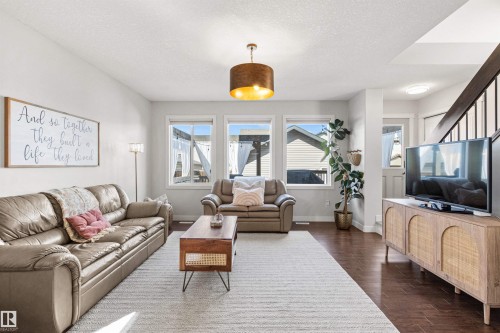 This living area features rich hardwood flooring, light-colored walls, and a contemporary ceiling light fixture - 38 Hewitt Circle, Spruce Grove, AB - Indoor Photo Showing Living Room