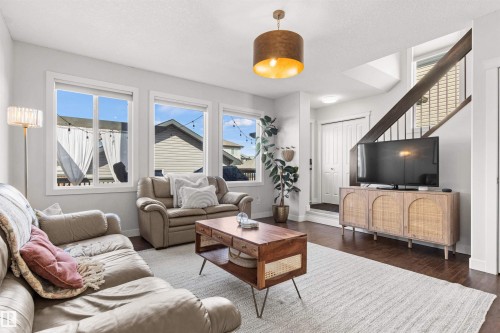 The living area features hardwood flooring, a staircase with dark banisters, and a contemporary light fixture - 38 Hewitt Circle, Spruce Grove, AB - Indoor Photo Showing Living Room
