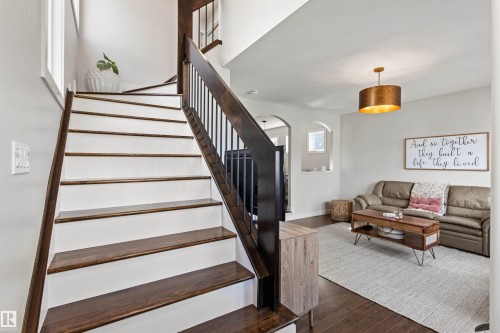 Inviting living area featuring hardwood floors, a staircase with dark wood treads and a white risers, and a contemporary light fixture - 38 Hewitt Circle, Spruce Grove, AB - Indoor Photo Showing Other Room