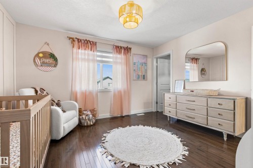 The room features rich hardwood flooring, a window with sheer pink and white curtains, and a light wood dresser with dark handles - 38 Hewitt Circle, Spruce Grove, AB - Indoor Photo Showing Bedroom