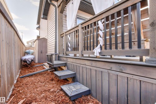 The property features a wooden deck with railing, accessible via wooden steps, with a fenced yard area covered in wood chips - 38 Hewitt Circle, Spruce Grove, AB - 