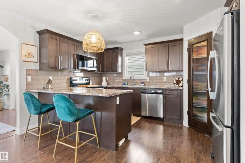 The kitchen features dark wood cabinetry, stainless steel appliances, a tiled backsplash, and a pantry with a glass-paneled door - 38 Hewitt Circle, Spruce Grove, AB - Indoor Photo Showing Kitchen With Stainless Steel Kitchen With Upgraded Kitchen