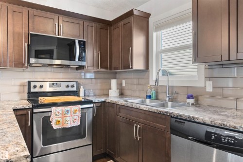 The kitchen features wood cabinetry, stainless steel appliances including a microwave, oven, and dishwasher, and a double basin sink - 38 Hewitt Circle, Spruce Grove, AB - Indoor Photo Showing Kitchen With Stainless Steel Kitchen With Double Sink With Upgraded Kitchen