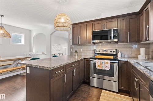 The kitchen features dark wood cabinetry, stainless steel appliances, a tile backsplash, and a spacious island with a countertop - 38 Hewitt Circle, Spruce Grove, AB - Indoor Photo Showing Kitchen With Stainless Steel Kitchen With Upgraded Kitchen