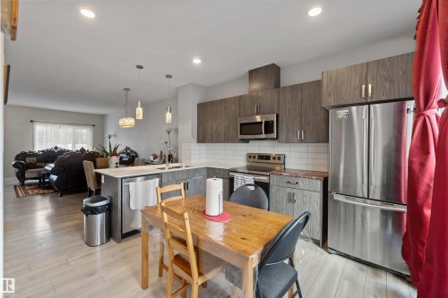 The kitchen features stainless steel appliances, grey wood-look cabinetry, a subway tile backsplash, and light-toned flooring - 2725 Orchards Road, Edmonton, AB - Indoor Photo Showing Kitchen With Stainless Steel Kitchen With Upgraded Kitchen