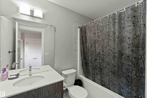 The bathroom features a vanity with a white countertop and an integrated sink, a wall-mounted mirror with lighting overhead, a toilet, and a shower-tub combination - 2725 Orchards Road, Edmonton, AB - Indoor Photo Showing Bathroom