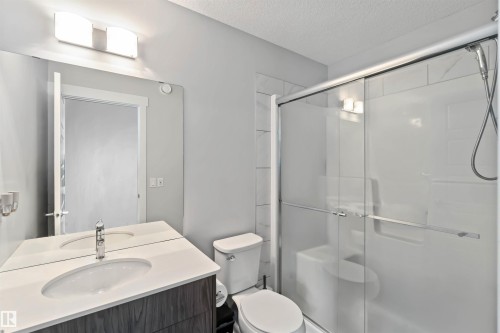 Bathroom featuring a vanity with a white countertop and an integrated sink, a large mirror, a toilet, and a glass-enclosed shower with a handheld showerhead - 2725 Orchards Road, Edmonton, AB - Indoor Photo Showing Bathroom