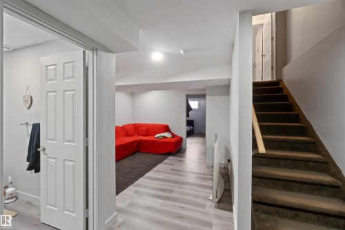 The property features a spacious room with light-toned flooring and a dark rug, along with a staircase leading upwards - 2725 Orchards Road, Edmonton, AB - Indoor Photo Showing Other Room