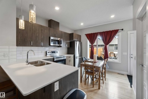 The kitchen features dark wood cabinetry, white countertops, and stainless steel appliances, including a microwave, stove, and refrigerator - 2725 Orchards Road, Edmonton, AB - Indoor Photo Showing Kitchen With Stainless Steel Kitchen With Double Sink With Upgraded Kitchen