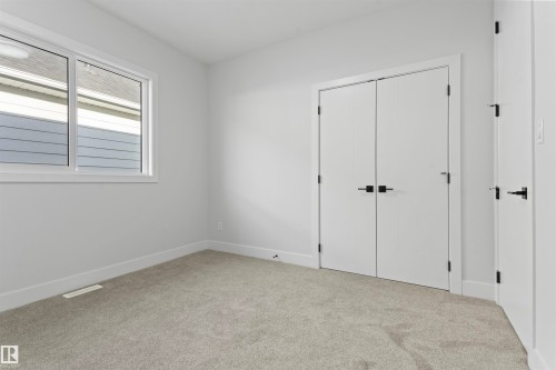 The property features a room with light grey walls, carpeted flooring, and a large window providing natural light - 156 Wyatt Ridge, Fort Saskatchewan, AB - Indoor Photo Showing Other Room