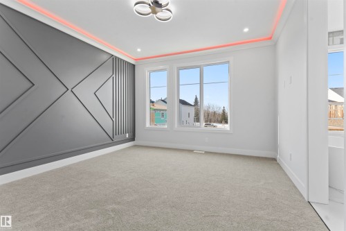 This room features a decorative accent wall with geometric paneling, light-colored carpeting, and three large windows providing natural light - 156 Wyatt Ridge, Fort Saskatchewan, AB - Indoor Photo Showing Other Room