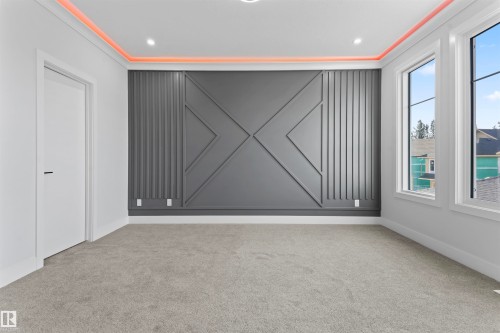 This room features a textured accent wall with geometric paneling, recessed lighting, and soft grey carpeting - 156 Wyatt Ridge, Fort Saskatchewan, AB - Indoor Photo Showing Other Room