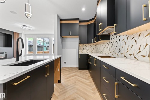 The kitchen features dark cabinetry with gold hardware, light countertops, and a striking patterned backsplash - 156 Wyatt Ridge, Fort Saskatchewan, AB - Indoor Photo Showing Kitchen With Double Sink With Upgraded Kitchen