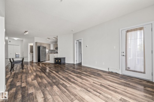 This inviting open-concept living area features wood-look flooring and light-colored walls, providing a bright and airy atmosphere - 212 10611 117 Street, Edmonton, AB - Indoor