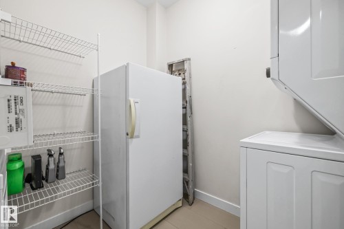 Utility space featuring a white freezer, wire shelving, and a stackable washer and dryer - 212 10611 117 Street, Edmonton, AB - Indoor
